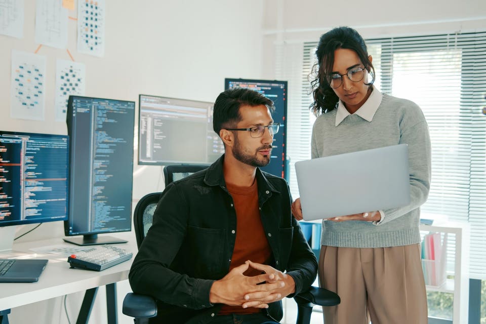 Hispanic Programmers Reviewing Code on Laptop in Modern Office