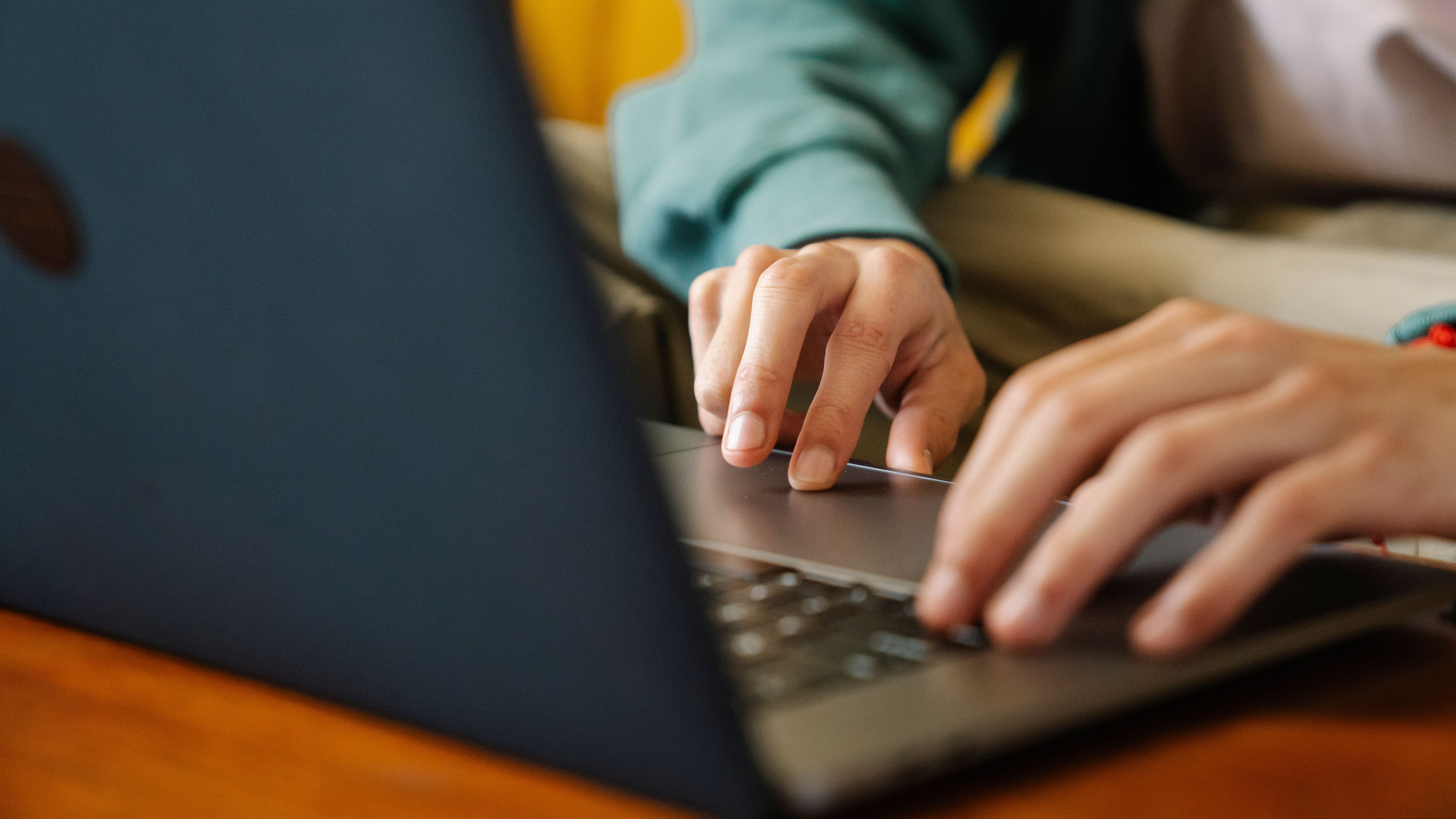 An individual typing on a laptop, focusing on the hands and keyboard in an indoor setting.