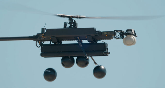 Anduril Industries Ghost-X drone dropping fire retardant balls in a test of fire suppression capability. The single-rotor drone is seen in side profile with four balls just starting to fall.