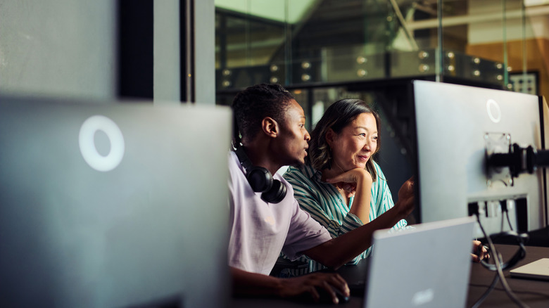 Two people working together at desktop computers in an office.